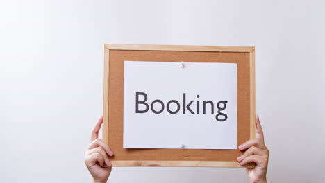 woman's hand shows the paper on board with the word booking in white studio background with copy space