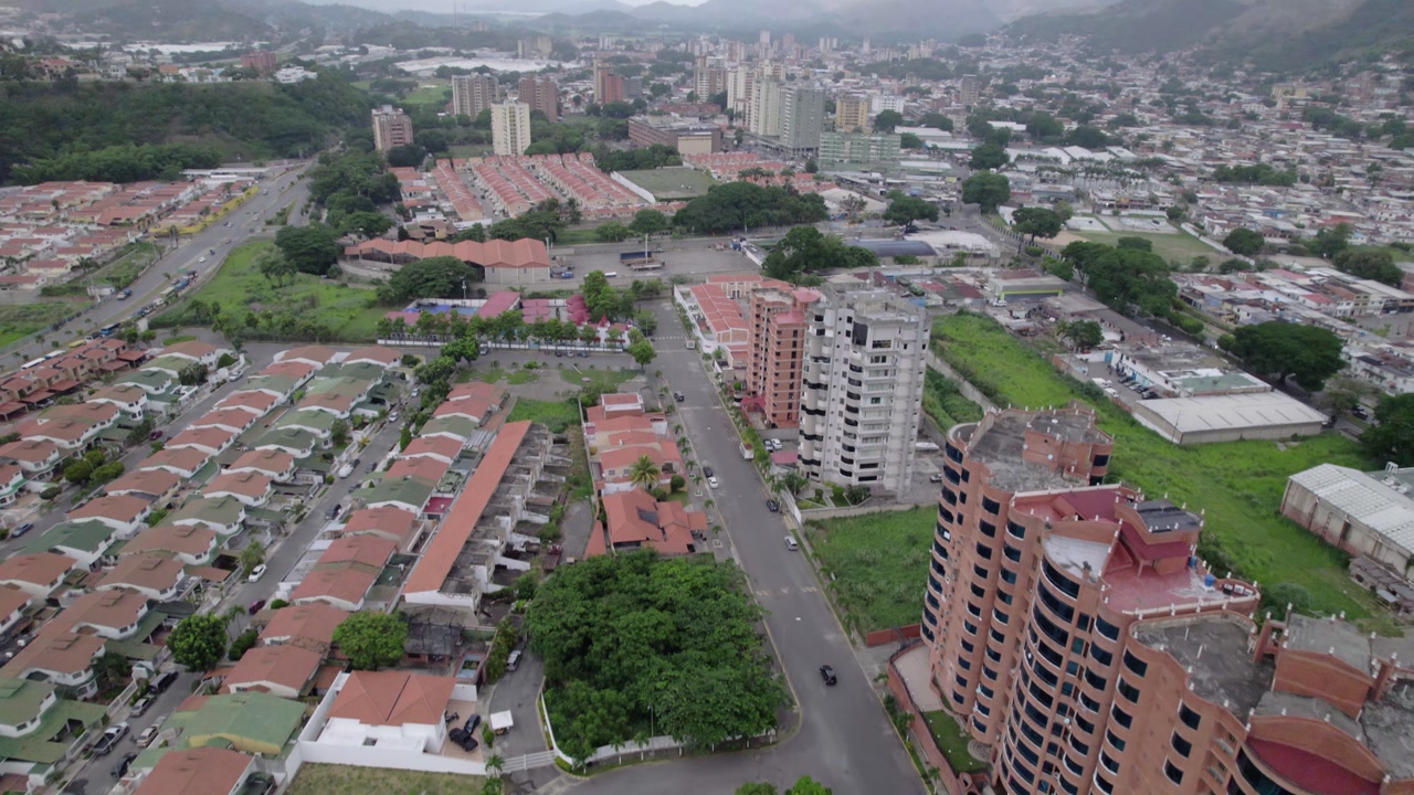documentary-style drone shot reveals a row of diverse houses and a busy road in an urban valley.