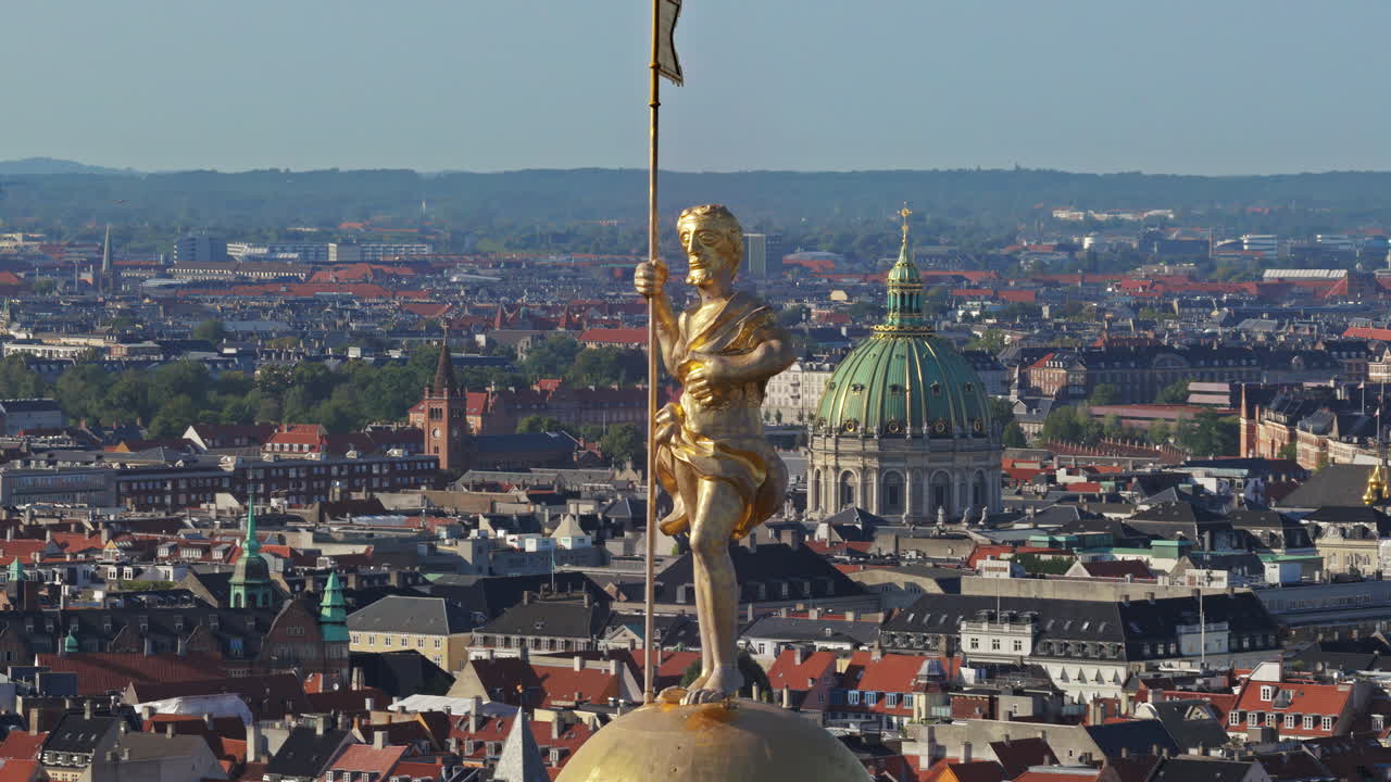 Aerial drone view of the golden statue atop a sphere on the Church of Our Saviour overlooking the Copenhagen skyline, with Frederik's Church dome in the background in Denmark