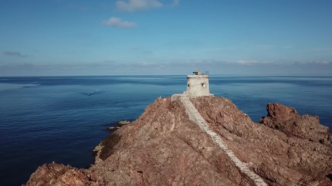 Ripresa cinematografica con drone di un'isola rocciosa solitaria al largo della costa di Nador, Marocco, circondata da calme acque blu del Mediterraneo.