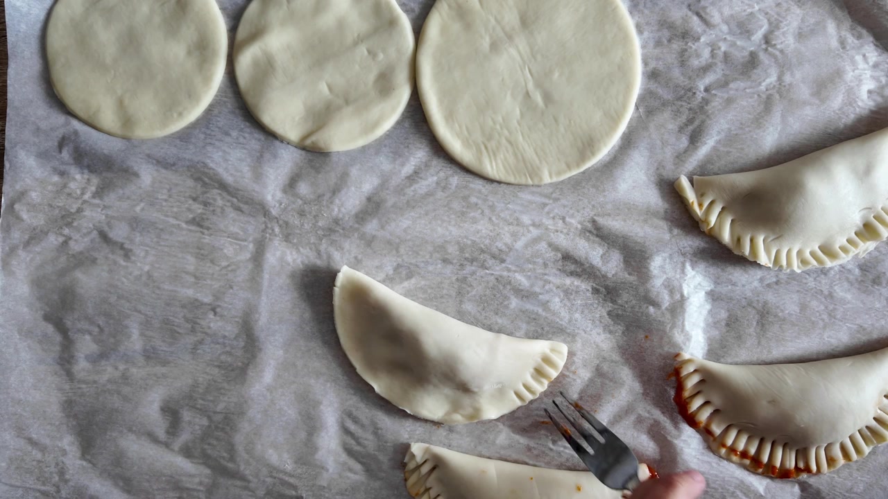 Madre e hija preparando empanadas de atún juntas, manos cocinando en la cocina de casa.