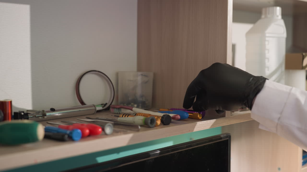 una vista de cerca de varias herramientas de laboratorio ordenadamente dispuestas en un estante, con una mano con guante seleccionando un artículo en el estante