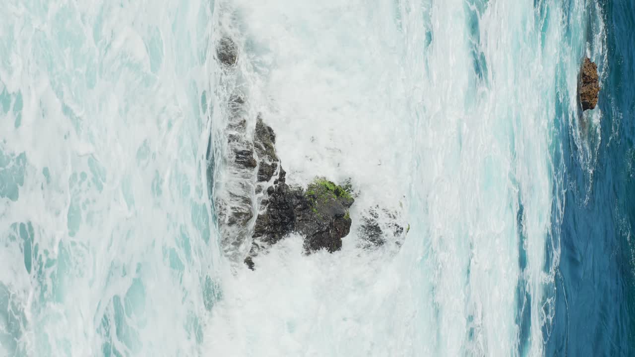 Splashes of water swallowing the rock in the middle of the sea in Tenerife, Spain, vertical static closeup slow motion