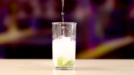 a glass fills with ice, lime, and liquid, capturing the essence of a mojito cocktail in a vibrant setting