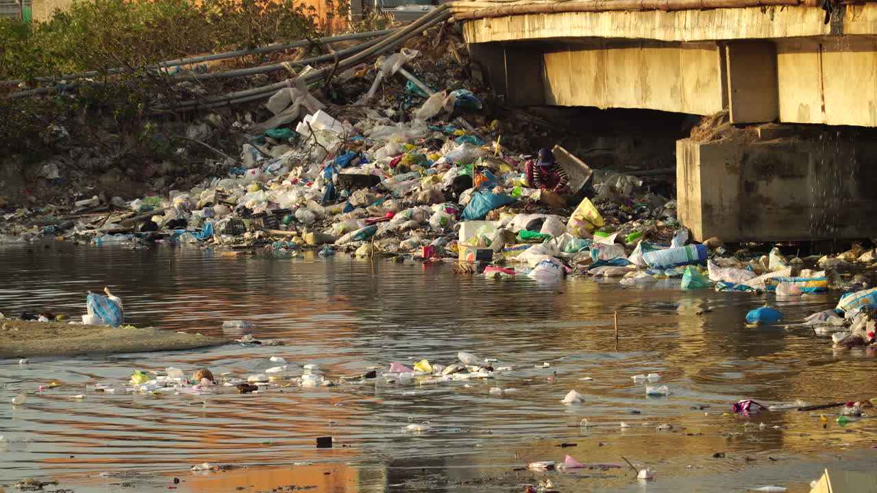 A Local In Son Hai, Vietnam Scavenge The Pile Of Garbage In The Riverside With Floating Waste Materials On The Water Surface