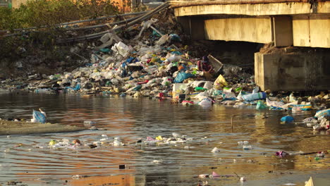 A-Local-In-Son-Hai,-Vietnam-Scavenge-The-Pile-Of-Garbage-In-The-Riverside-With-Floating-Waste-Materials-On-The-Water-Surface