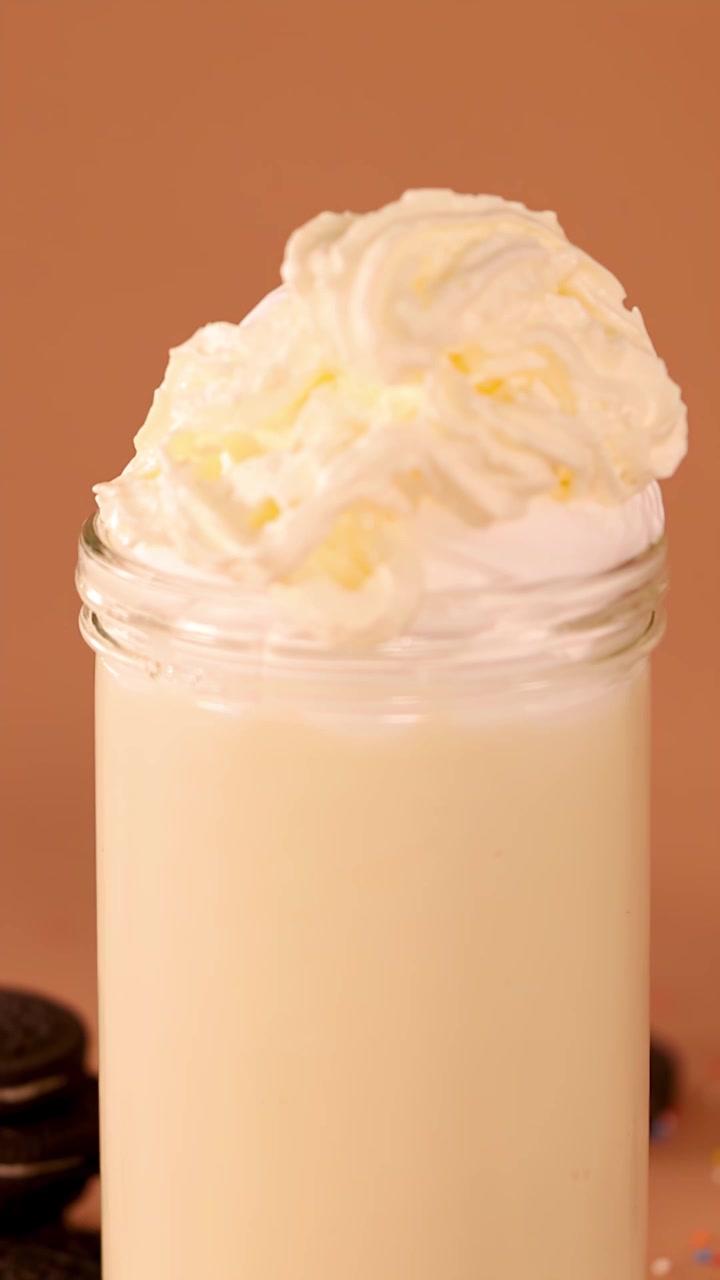 Primo piano di milkshake alla vaniglia in barattolo di vetro con un vortice di panna montata su sfondo caldo