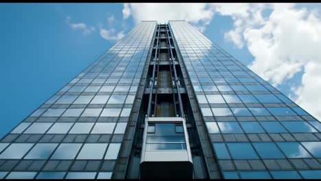 a vertical perspective of contemporary architecture showcasing a sleek glass facade and an elevating lift against a clear sky