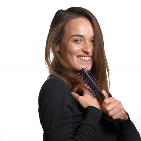 smiling lady in black jumper and with long hair is holding a hairbrush in the studio on a white background.