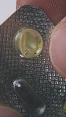 sick person taps with little bright yellow pill blister on light surface extreme close view