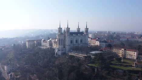 Basilica-of-Notre-Dame-De-Fourviere,-Lyon,-France-aerial-view-across-hazy-sunrise-city-landscape