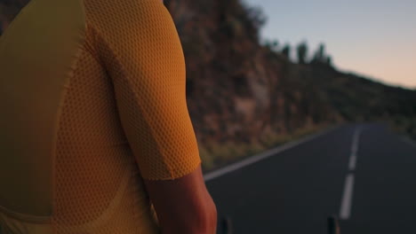 sports enthusiast, dressed in yellow t-shirt and gear, sits on bike on mountain top, gazing at mountains and sunset after workout