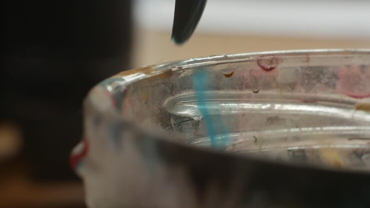 Pulire il pennello sul bordo di un barattolo di vetro dall'acqua in eccesso durante il processo artistico, primo piano