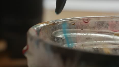 wiping paintbrush on the edge of glass jar from excess water in artistic process, closeup