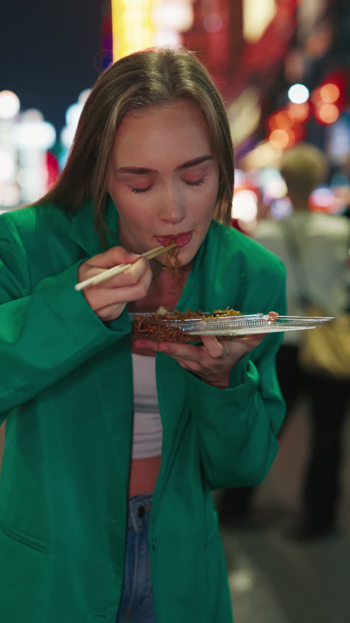 Donna che mangia noodles in un mercato notturno