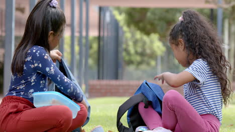in school, two girls sitting on grass unpacking backpacks during break time