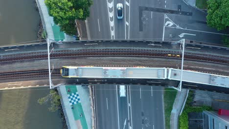 Von-Oben-Nach-Unten-Stationäre-Drohnenaufnahme-Eines-Zuges,-Der-über-Einer-Stark-Befahrenen-Straße-Vorbeifährt