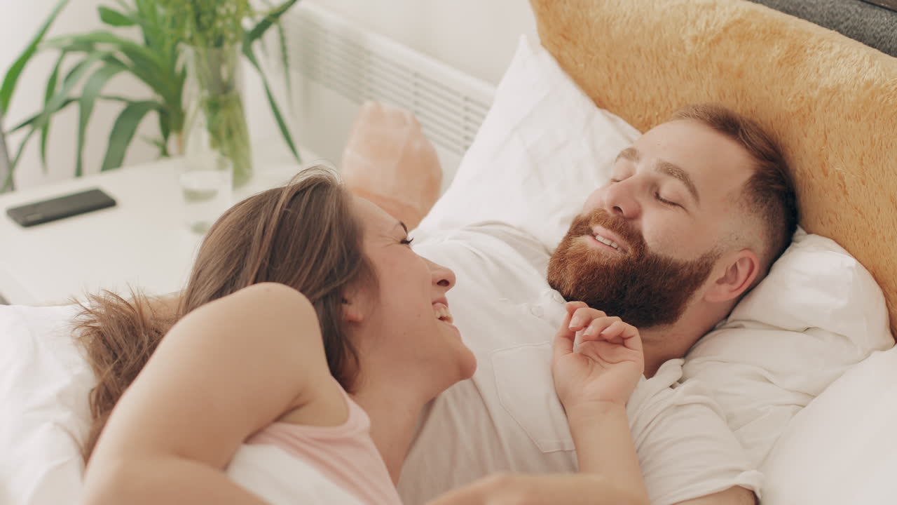 Blije vrouw kijkt naar haar slapende partner in bed