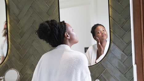 young african american woman examines her skin in a mirror at home