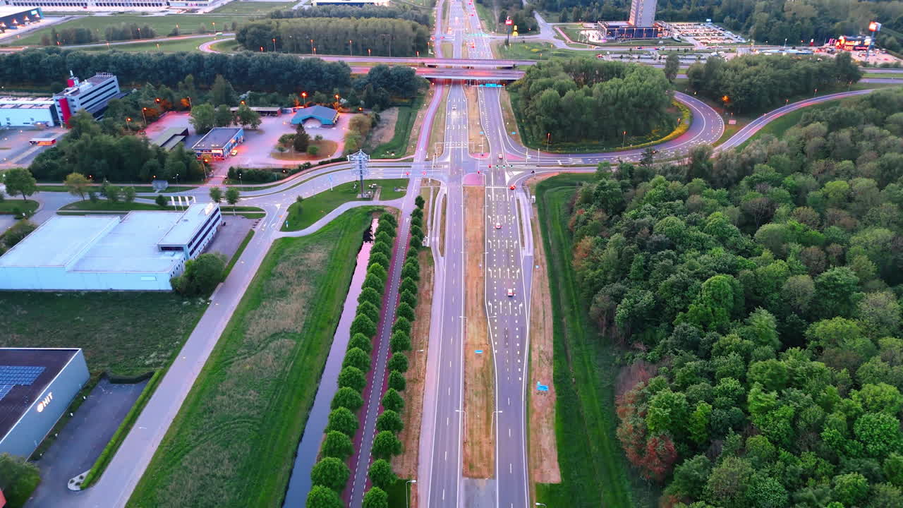Sunset over busy intersection. Traffic flows through a complex intersection surrounded by green trees and urban buildings during the evening twilight