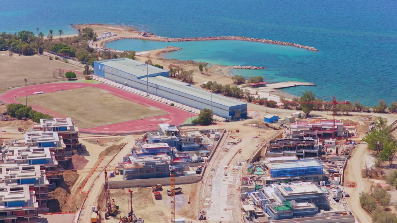 Impressionante prospettiva aerea di un cantiere edile su larga scala che sviluppa un moderno complesso residenziale o un resort con più edifici, gru e macchinari pesanti lungo una splendida costa