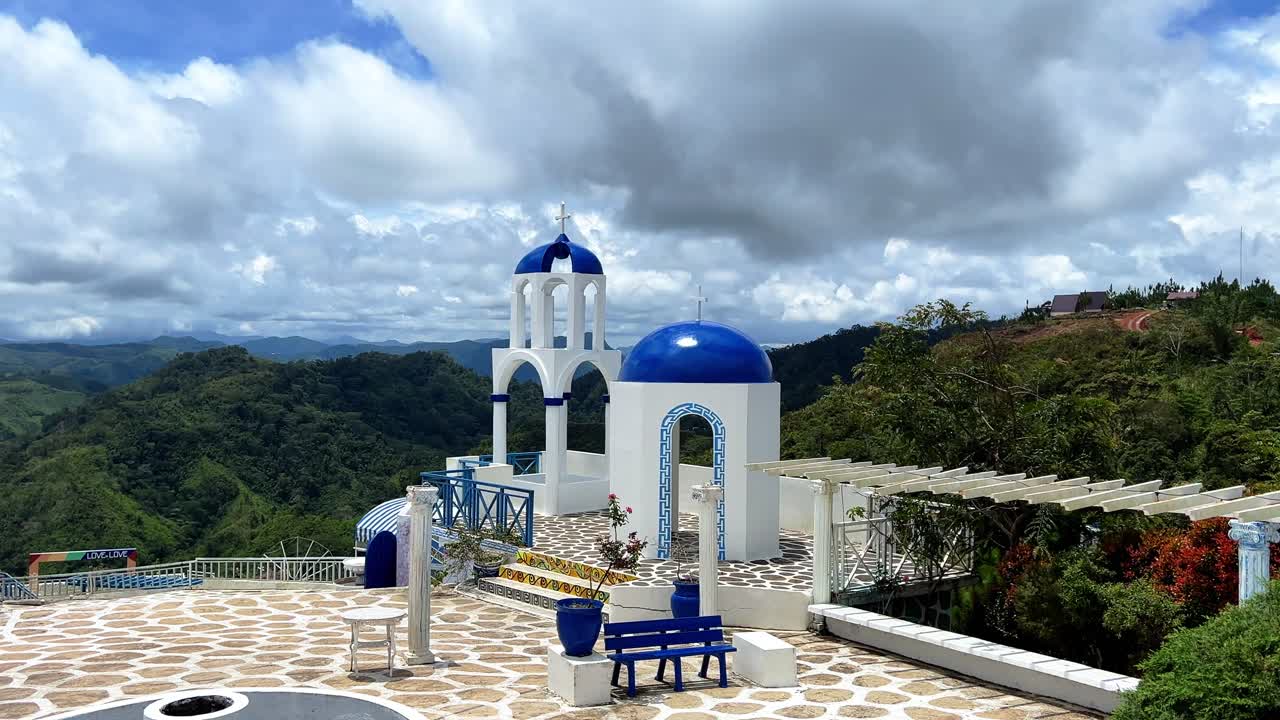 Santorini-style white domes and arches set against lush green mountains and cloudy sky. Ideal for travel, romance, or cultural visuals