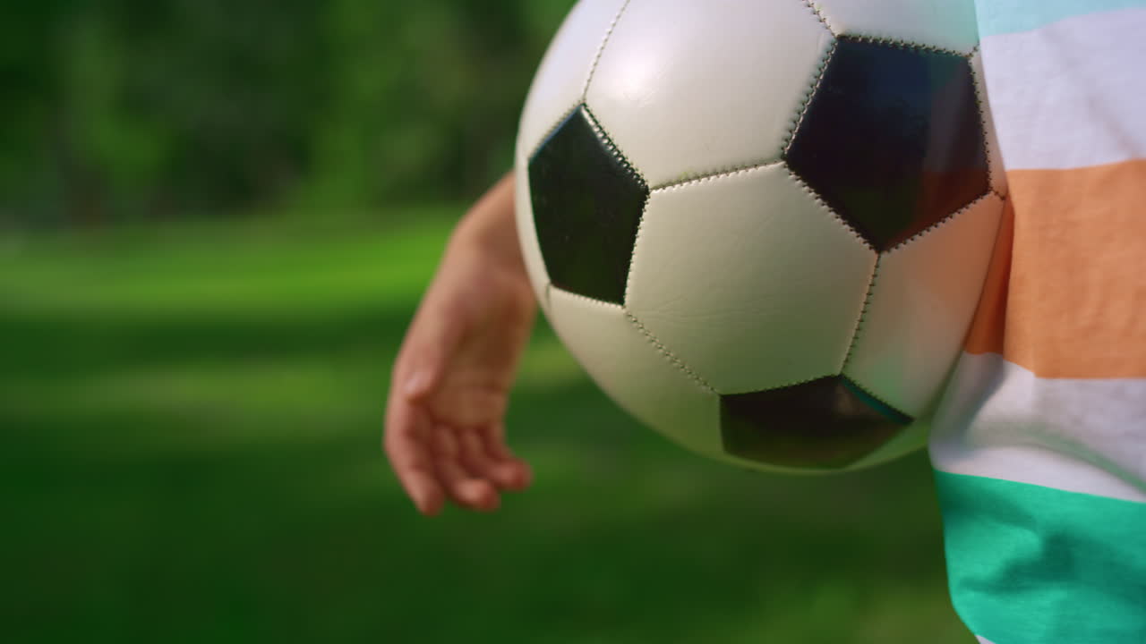 Fodbold i hånden på ung sportsmand i parken, tæt på. Ukendt dreng holder bolden.
