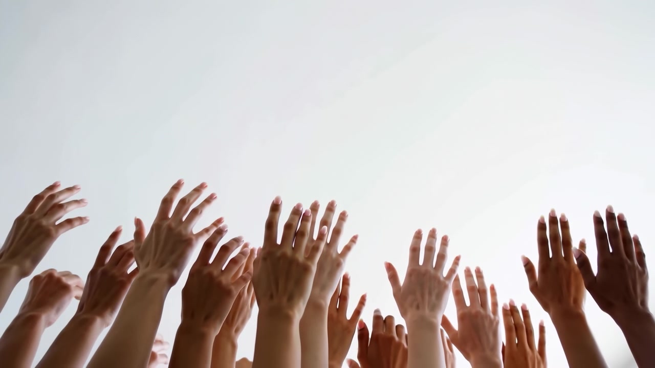 Raised crowd of diverse hands reaching upward from low angle, palms open against soft gray background with generous negative space, showing unity, support, hope, and collective energy