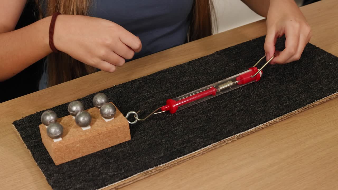 A person uses a spring scale to measure frictional force on a weighted block sliding over a carpeted surface
