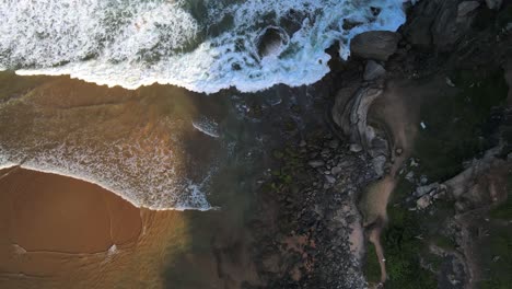 Aerial-view-of-waves-crashing-into-a-rocky-shoreline-in-Geriba-Beach,-Buzios,-Brazil