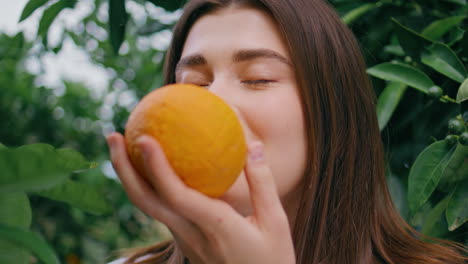 closeup woman picking orange lush greenery farmland. happy lady sniffing citrus