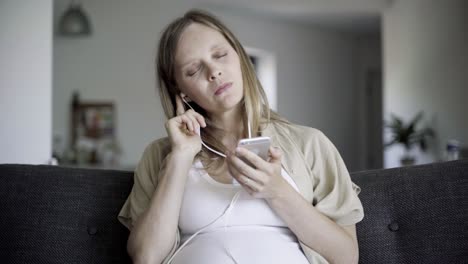 front view of happy pregnant woman choosing, listening to music