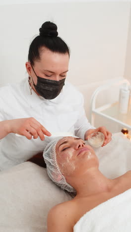 esteticista aplicando una máscara de crema hidratante química médica en el rostro de una mujer joven adulta