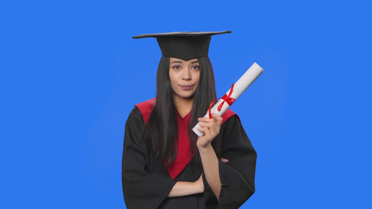retrato de una estudiante en traje de graduación mirando pensativamente su diploma, luego se regocija de que hay una idea. joven posando en el fondo de la pantalla azul. de cerca. cámara lenta lista 59.94fps