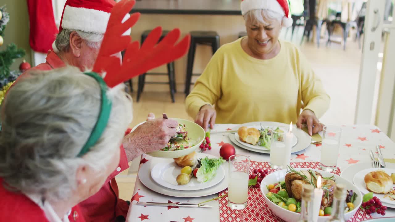 grupo de felices amigos mayores caucásicos en sombreros de santa comiendo la cena de navidad juntos en casa