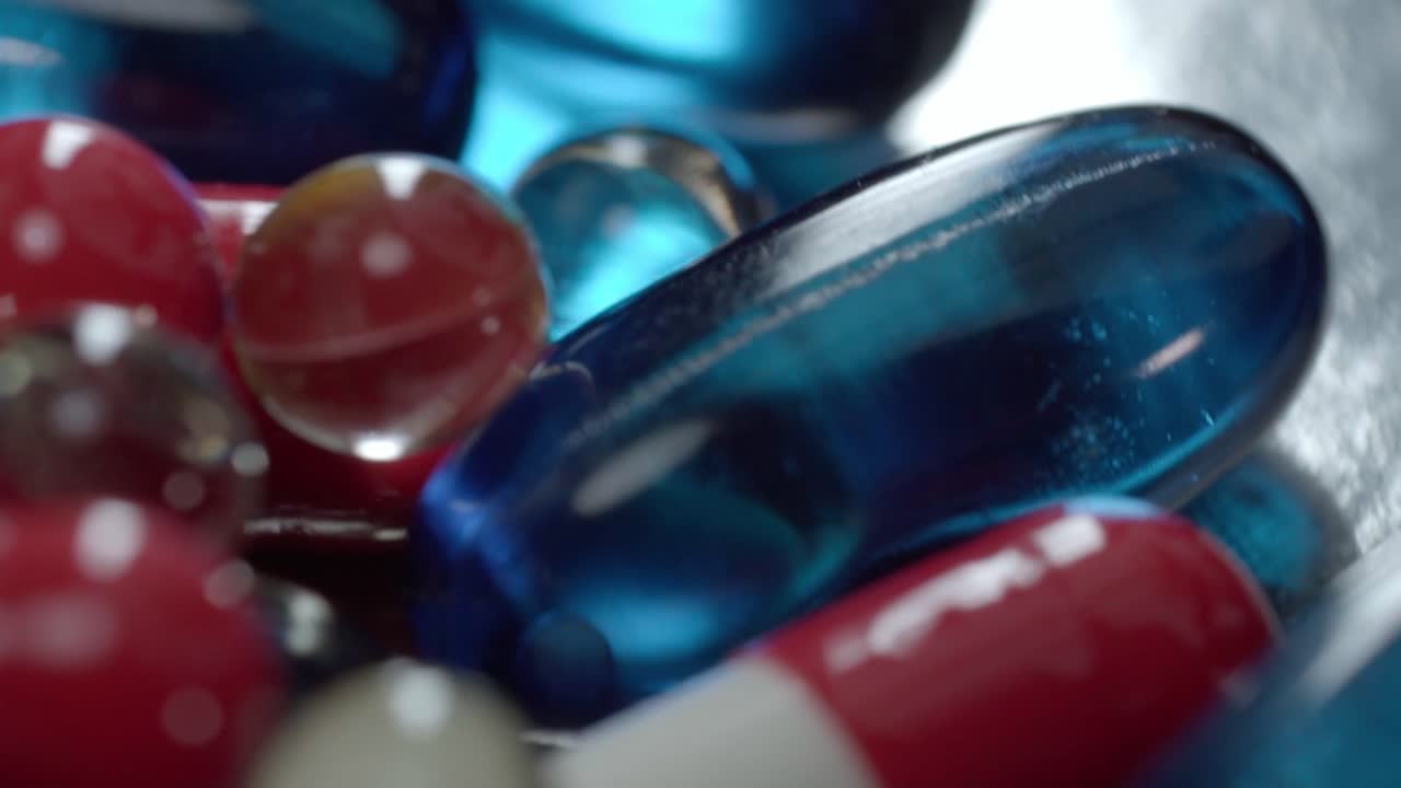 Macro shot of assorted medicine capsules and gel pills on reflective surface under studio lighting
