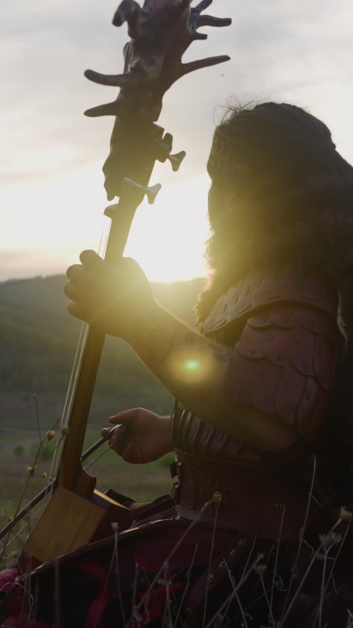 Folk musician plays tovshuur with bow in large mountain valley at back light side view. Meditative music of native Siberian tribes. Ethnic festival