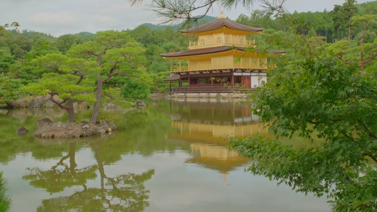 Static shot of Kyoto iconic Golden Pavilion reflected in a tranquil pond with gentle rippling water in the foreground. A peaceful view of traditional Japanese architecture and serene landscape.