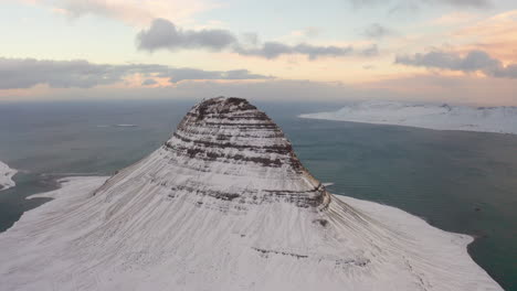 aerial drone shot showing snowy kirkjufell mountain and icelandic fjord in background during sunrise in iceland