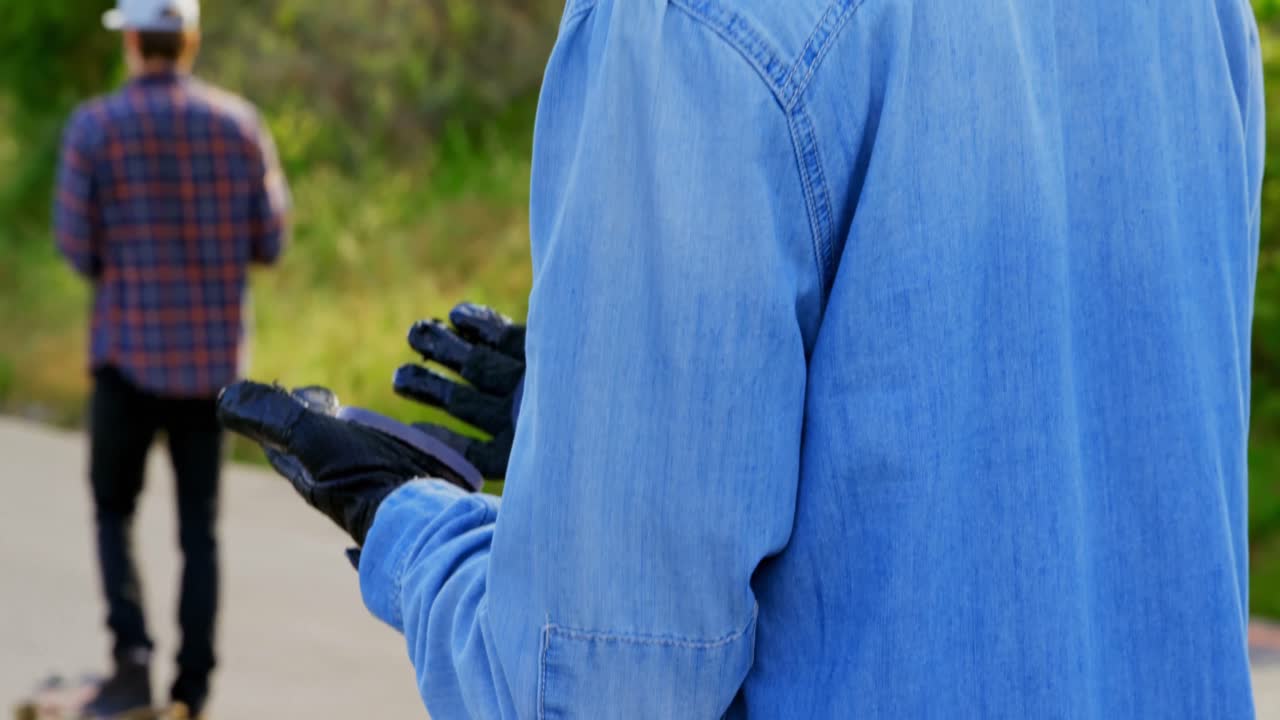 боковой вид молодого кавказского скейтбордиста, смотрящего на свои перчатки для скейтборда на сельской дороге 4к