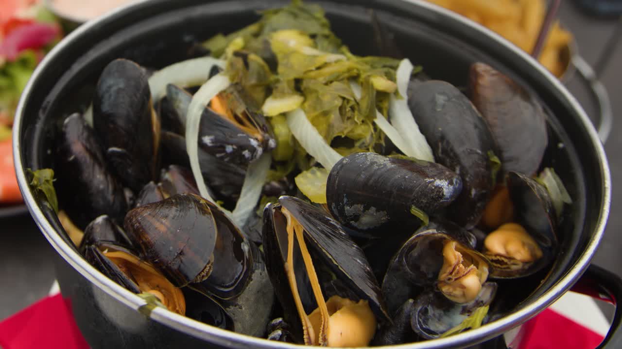 Steaming mussels with fries and salad on sunlit restaurant table, shallow depth of field