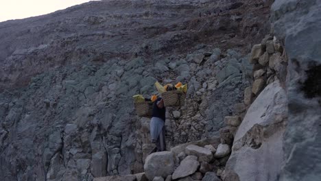 laborer ascends rocky slope with large sulfur load from ijen crater under harsh rocky conditions, medium tracking