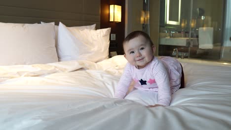 hermosa niña bailando arrastrándose en la cama blanca de la habitación del hotel por la noche después del check-in