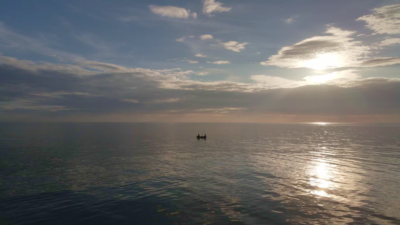 Riprese aeree con drone in orbita dell'oceano in silhouette al tramonto con una piccola barca da pesca e il suo riflesso sul mare.