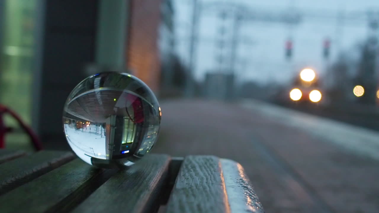 Krystallkule på en benk reflekterer et tog som passerer på stasjonen.