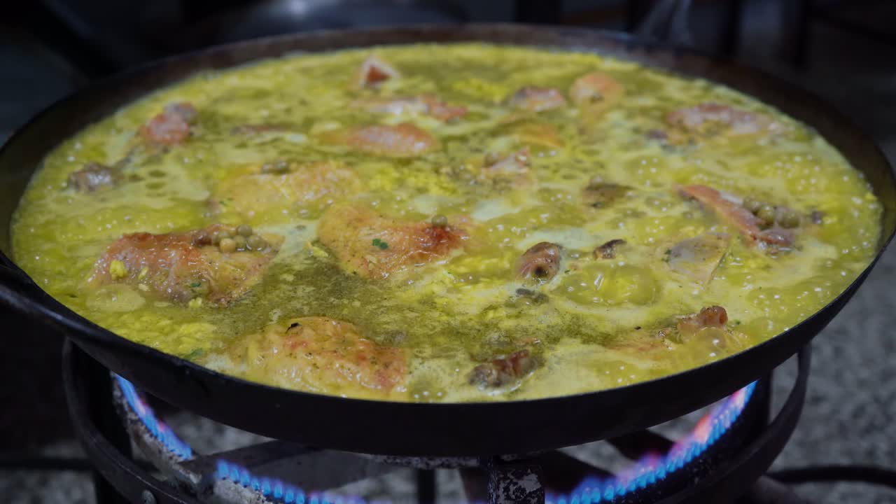 Pollo che sobbolle in un grande wok a fuoco medio per la paella spagnola, primo piano.