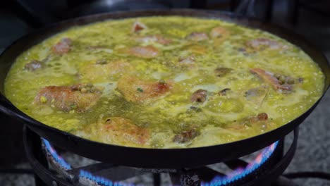 simmering chicken in a large wok over medium heat for spanish paella, close up