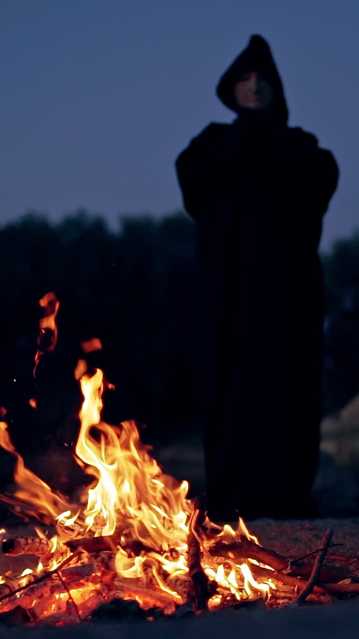 Sad monk by the fire. Man in cassock leans toward the fire at night Vertical video