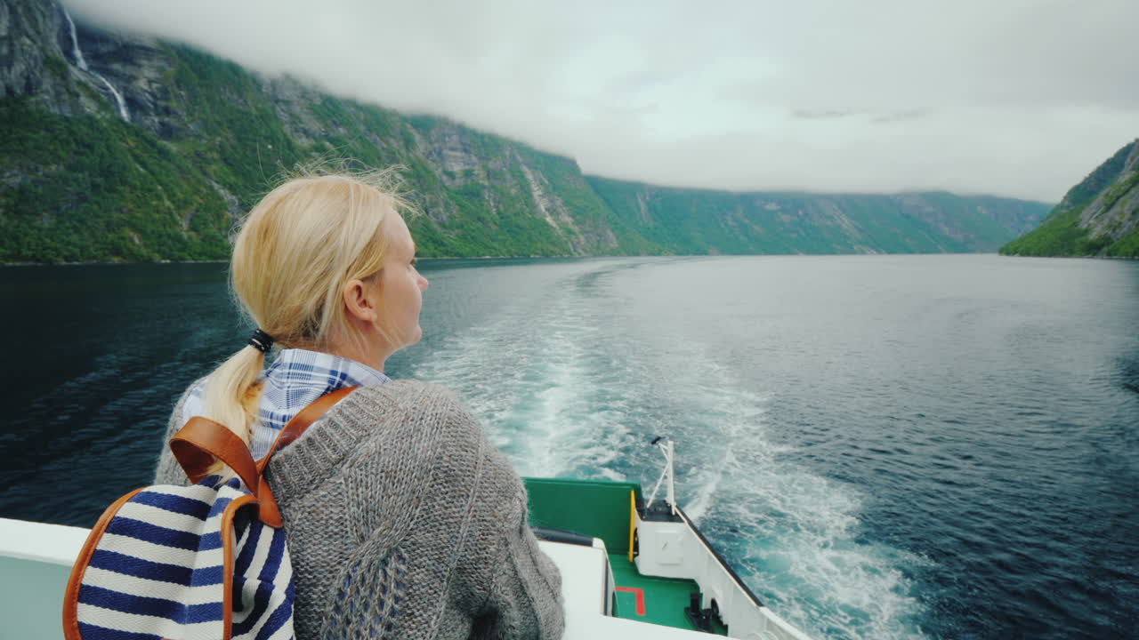 Turistkvinde beundrer den maleriske norske fjord fra agterstavnen af et krydstogtskib.