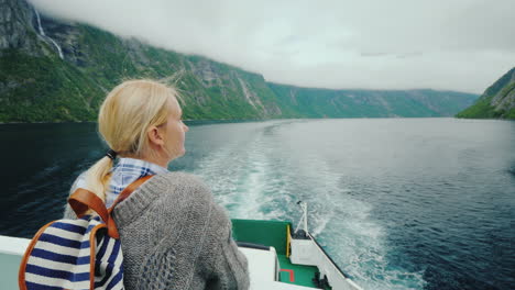 Tourist-Woman-Admiring-The-Picturesque-Norwegian-Fjord-From-The-Stern-Of-A-Cruise-Ship